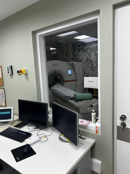 Leaded glass window onto the examination room, with a two-monitor workstation.